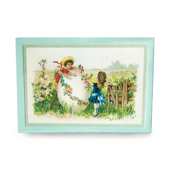 Elegant vintage-inspired Easter wood block made with end-of-19th-century postcard. Decorate your home or gift to a friend this elegant reminder of what it was like to send Easter postcards to relatives and friends! Reproduced vintage “Easter Greetings” postcard. Easter Vintage Decorations. Elegant illustration features young girl and boy decorating an Easter egg in the meadow. Easter egg garland on postcard used to create elegant border on sides of wood block. tribegift.com