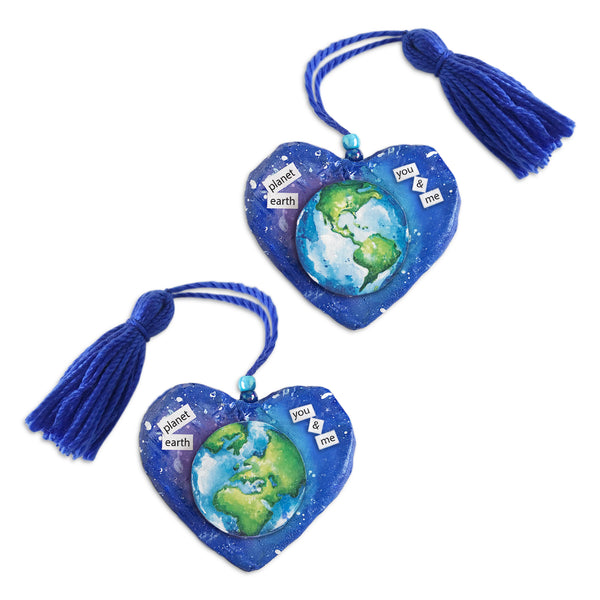 Heart paper mache sculpture celebrates planet earth and world peace. Perfect peace gift uniquely created to fit in palm of hand. One-of-a-kind hand sculpted and hand-painted shape. Earth divided into two halves with hemisphere on each side of heart. Color selection promotes sustainable global awareness that encourages us to respect, protect and preserve planet earth and the cosmos. Earth illustration suspends up from outer-space-colored background. Deep blue yarn tassel attached. Tribegift.com
