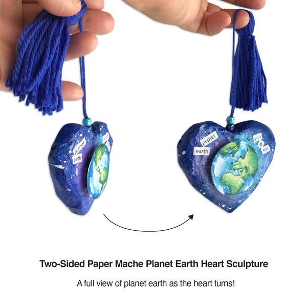 Heart paper mache sculpture celebrates planet earth and world peace. Perfect peace gift uniquely created to fit in palm of hand. One-of-a-kind hand sculpted and hand-painted shape. Earth divided into two halves with hemisphere on each side of heart. Color selection promotes sustainable global awareness that encourages us to respect, protect and preserve planet earth and the cosmos. Earth illustration suspends up from outer-space-colored background. Deep blue yarn tassel attached. Tribegift.com